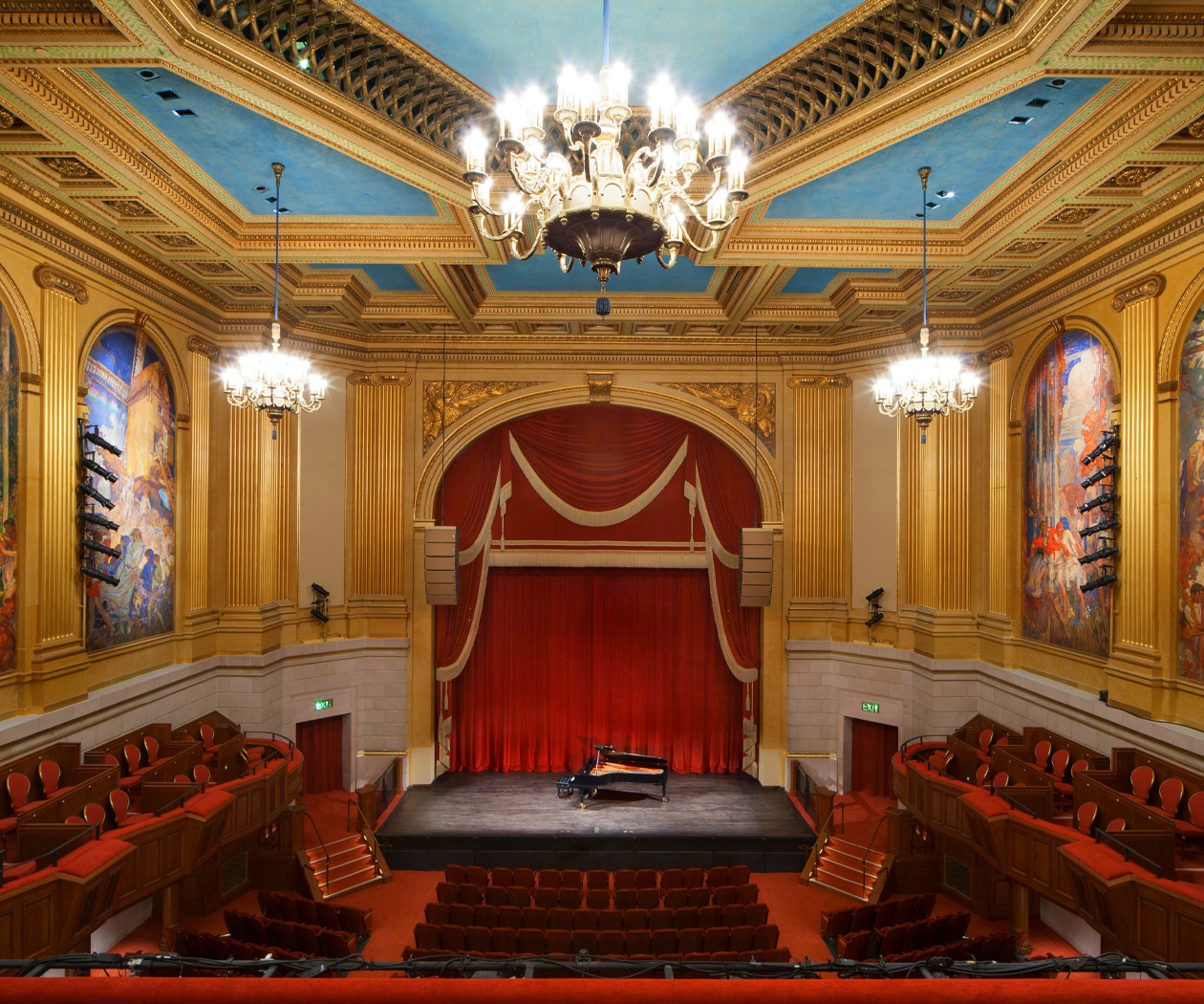 Interior of Herbst Theater in San Francisco, showing the ornate ceiling, chandeliers, red stage curtain, and seating